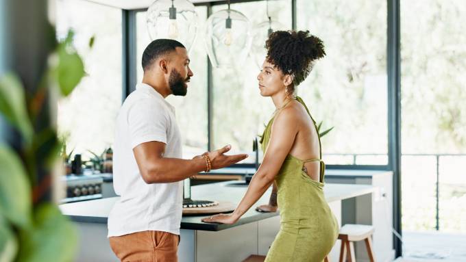 A man and woman standing in a fancy kitchen. The man is gesturing at the woman as they have a serious discussion.
