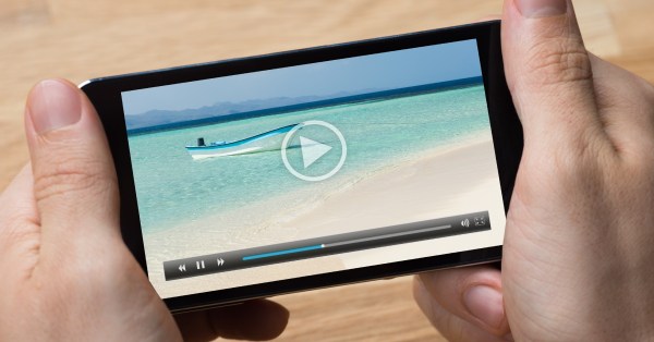 A man holding his smartphone and watching a movie. The movie is paused on a scene with a fishing boat in the water.