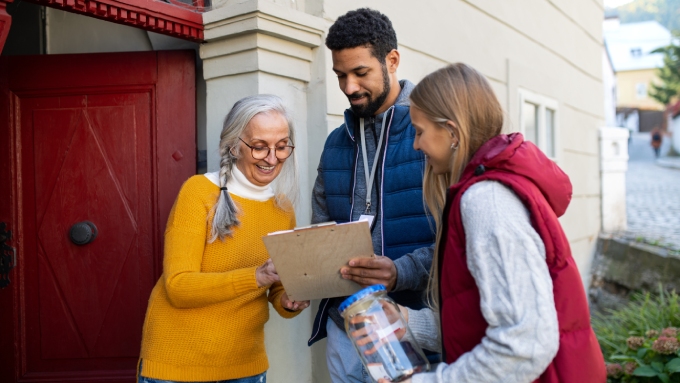 An older woman, a young man, and a young woman stand outside next to each other, looking at a clipboard.