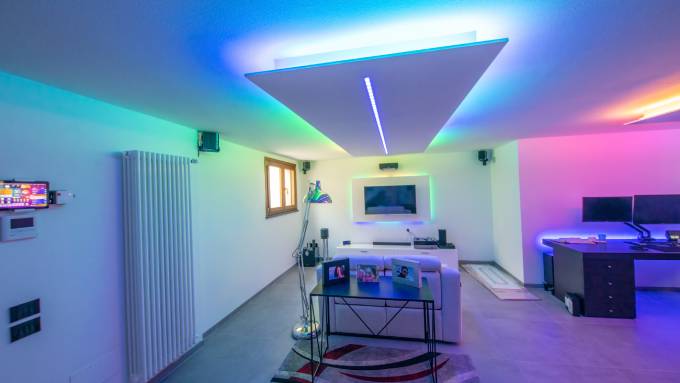 A basement game room set up with a movie area and a gamers area. There are also LED color-changing lights.