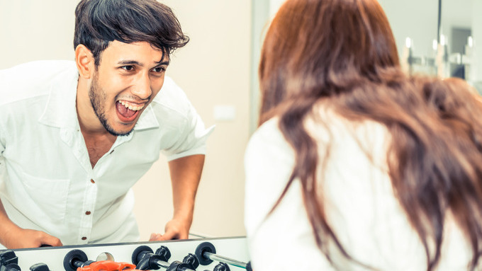 A young couple, male and female, stands on opposite sides of a foosball table, smiling and enjoying a friendly game together.
