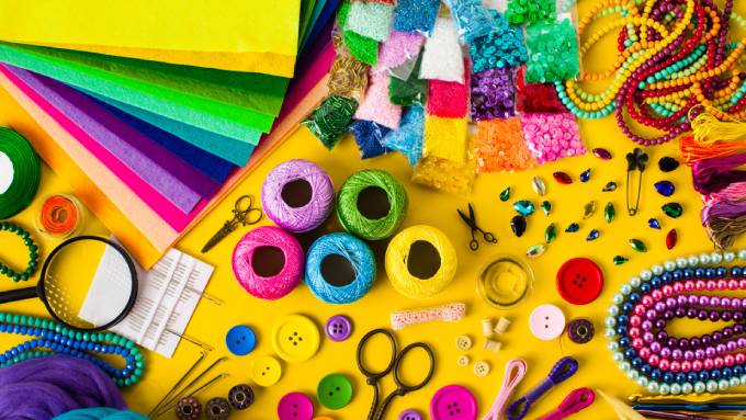 Colorful spools of twine, felt, beads, buttons, and tools like scissors and bobbins on a yellow background.