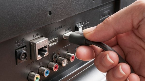 A close-up view of a person’s hand as they plug the end of an HDMI cable into a black TV’s HDMI 1 port.