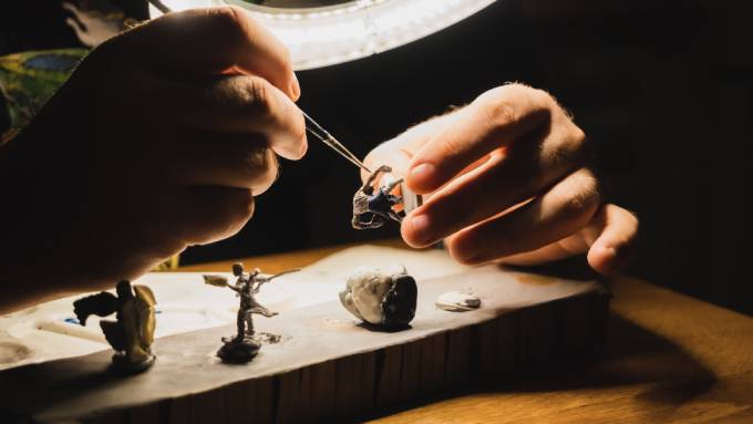 A person leaning over a table and looking through a magnifying glass with a ring light while painting miniatures.