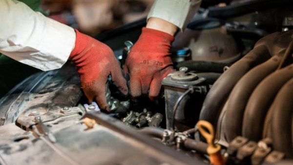 A person wearing red gloves, working on the engine of their vehicle. Their gloves look quite dirty.