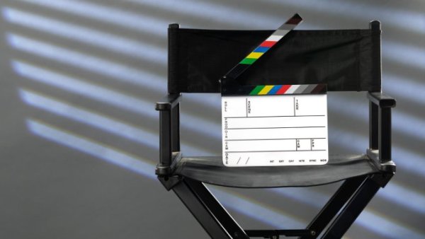 A black director's chair sits against a gray backdrop. A clapper sits on the director's chair.