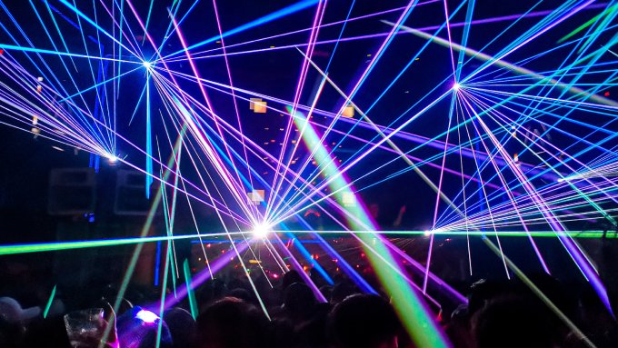 An array of lasers cast over a crowd at a nightclub. The lasers are mainly blue, purple, and green.