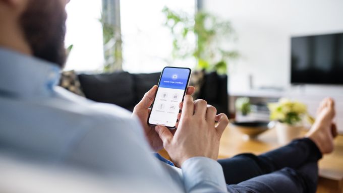 A close-up view shows a man holding a phone while sitting on a couch and resting his feet on a wooden coffee table.