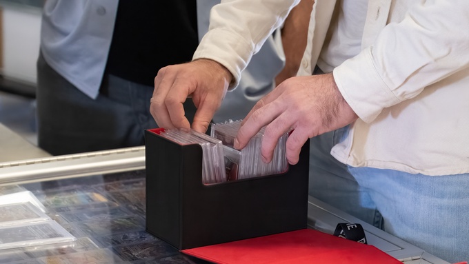 A person looking at graded collector’s cards in a black and red box. The box sits on a plastic case full of cards.