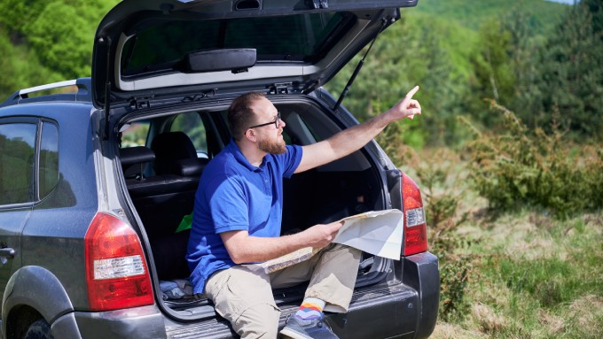 A person in a blue shirt sitting in the back of a hatchback vehicle and gesturing toward nature and the sky.
