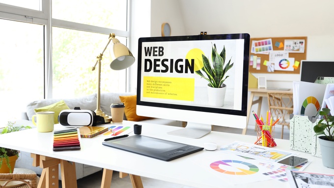 An artist's workstation with a computer screen showing the words "web design" and art materials on a white table.