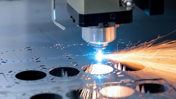 A close-up of a CNC milling machine cutting circles out of a thin sheet of metal with sparks flying off of it.