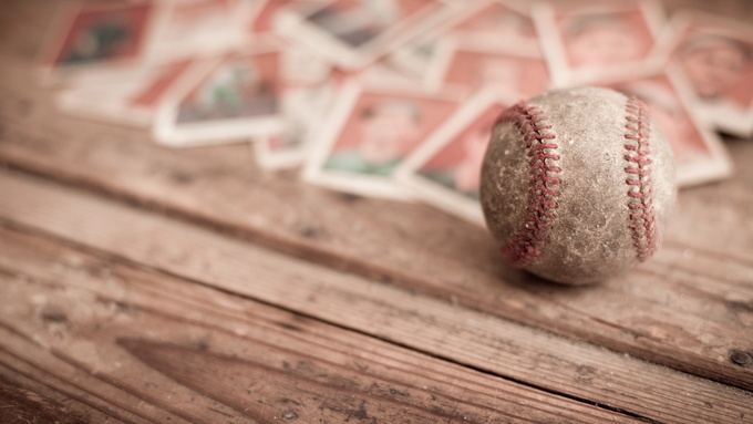 A close-up of a dirty baseball sitting on top of a wooden table. Behind it are blurred baseball cards.