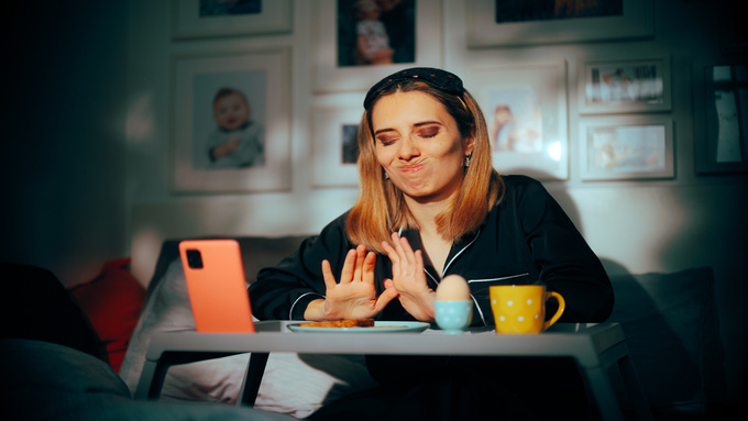 A person in their pajamas making an uncomfortable face while they push away a plate of breakfast that they don't want.