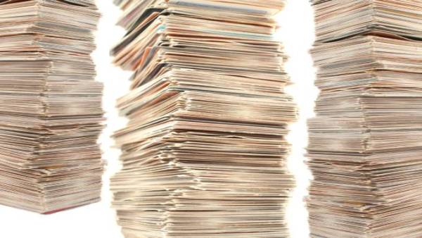 Three large stacks of mixed trading cards with colorful surfaces peeking through the sides of the untidy towers.