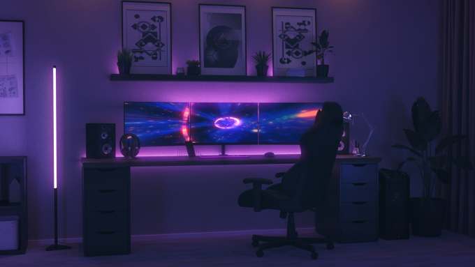 In a room, the lights are off except for bright neon lights behind some computer monitors on the desk.