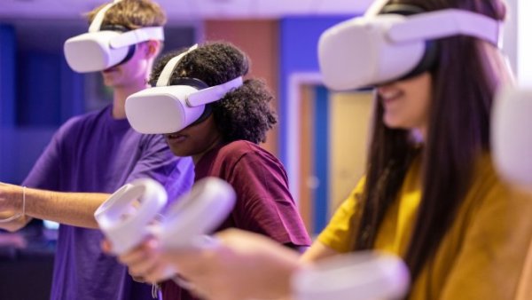 Three adults using gaming VR headsets in a large room. They are wearing headsets and using gaming controllers.