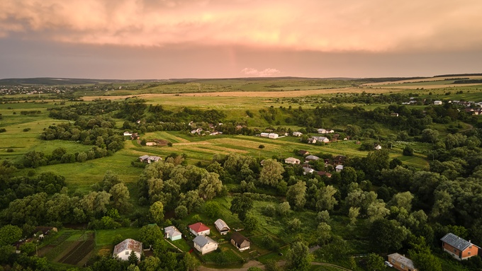 An aerial view shows a rural area with rolling hills, homes, mature trees, barns, and winding roads.