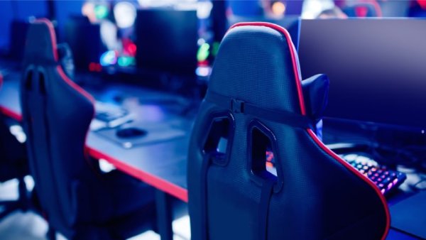 Multiple gamer chairs lined up in a row in front of tables with blank monitors and colored keyboards.