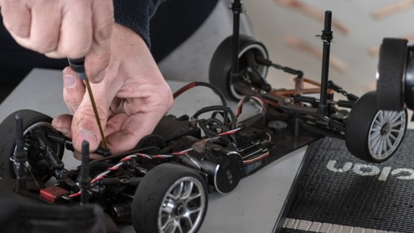 A person using a screwdriver to repair their RC car. The car is lying flat on a gray table with the cover removed.