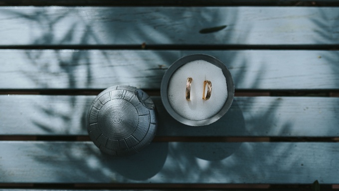 Two gold rings in a container filled with white sand, with the lid off. The lid resembles a Death Star from Star Wars.