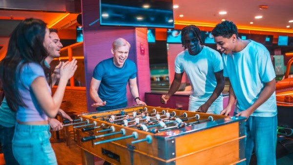 A group of men and women play foosball at an event venue. They are smiling, clapping, and appear to be having a great time.