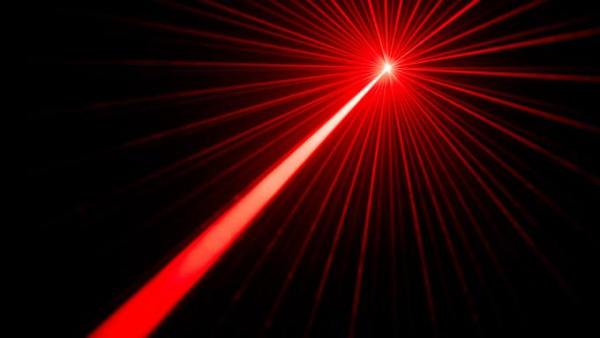 A red laser beam shoots upward at a 45-degree angle in front of a black background. Its tip breaks into several branches.