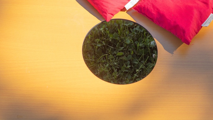 A close-up view of the hole of a cornhole board. The board is yellow, and there are a couple of red bags near the hole.