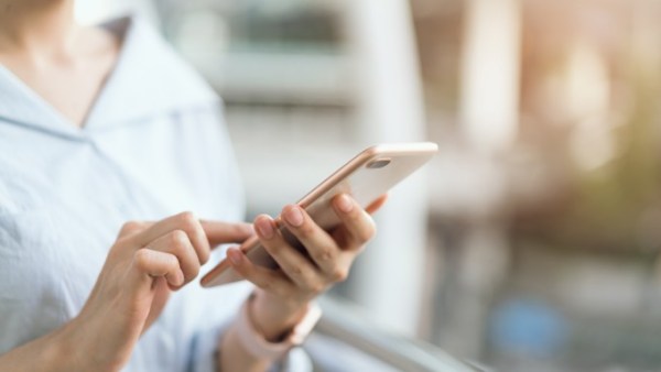 A close-up view shows a woman wearing a light blue shirt holding a smartphone and scrolling. The background is blurry.