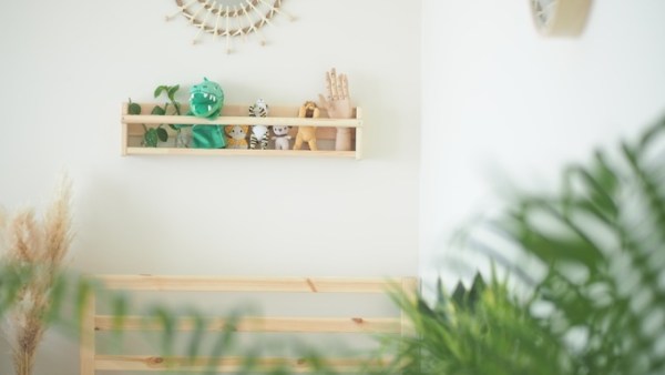 A decorative shelf displaying small stuffed animals and a posable wooden hand hangs on a white wall in a room.