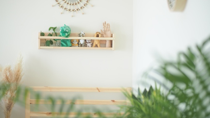 A decorative shelf displaying small stuffed animals and a posable wooden hand hangs on a white wall in a room.
