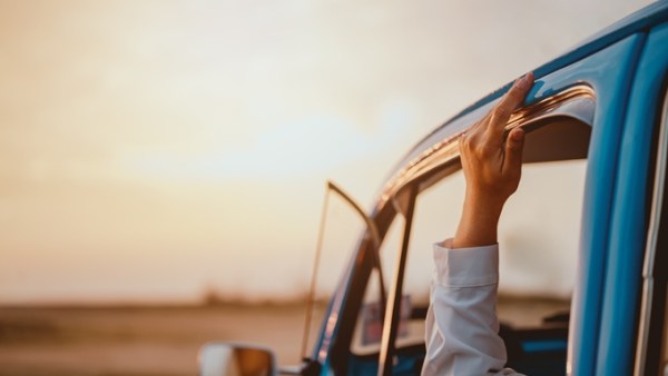 A person's arm rests on the edge of a blue vehicle's window ledge with their hand touching the top of the vehicle.