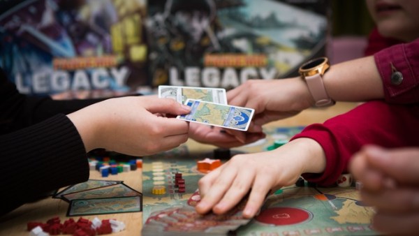 A tabletop game already in progress, with several people reaching over each other to grab cards and move pieces.