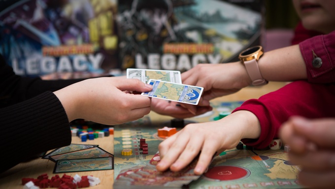 A tabletop game already in progress, with several people reaching over each other to grab cards and move pieces.