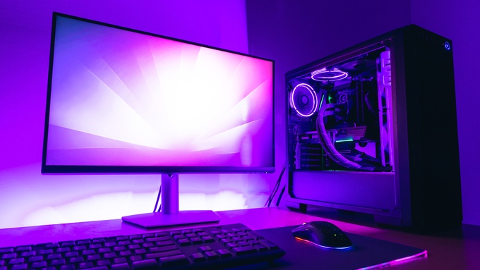 A desk with a monitor glows purple. A PC with a water cooling case sits beside the mouse, mousepad, and keyboard.