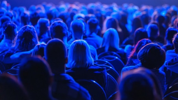 A large group of people sitting and watching something together. The room is dark, but there's a bright blue light shining.