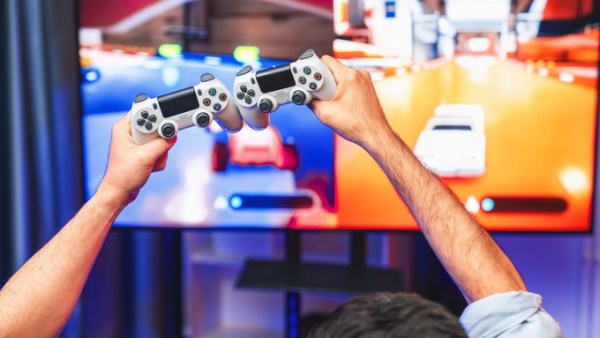 Two people raise their video game controllers in the air while playing a colorful racing game on a large screen.