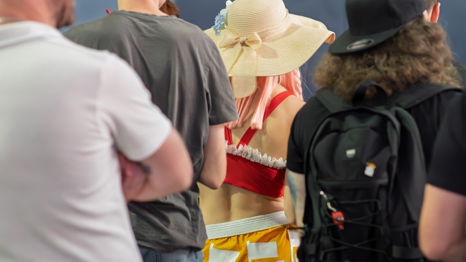 A group of anime fans standing in a convention center. One person is wearing a costume and a pink wig.