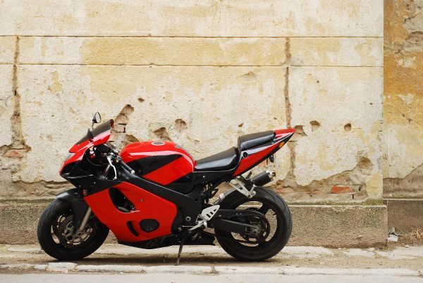 A sleek, glossy, modern black-and-red motorcycle parked beside a weathered beige building made of stone.