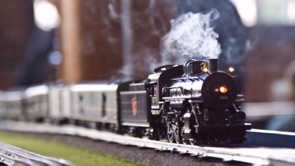A black model steam train on a model train track. A plume of steam is coming out of the train's smoke stack.