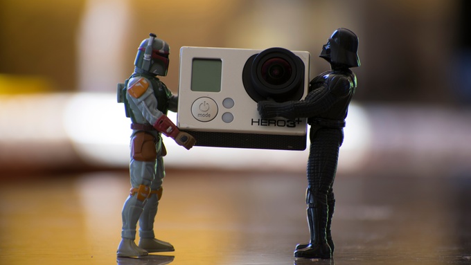 Two toy action figures standing on a glossy surface while holding a small white device between them.