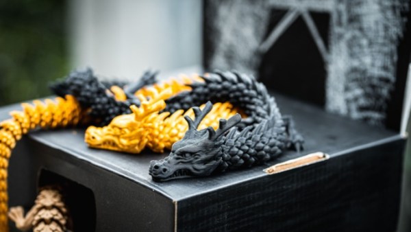 A close-up of four 3D-printed dragons on a black box. The dragons are solid black, yellow, and brown.