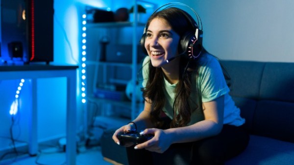 In a blue-lit room, a woman on a couch wears a headset and holds a gaming controller. A computer tower is beside her.